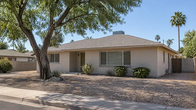 Small late-1940s early ranch-style home in an older Tempe, Arizona neighborhood with a low-pitched hip roof covered in new composition shingles, painted block walls, a mature shade tree and a gravel yard