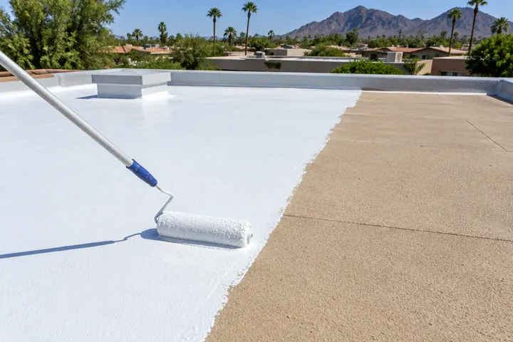 Roller applying bright white elastomeric coating over a tan foam flat roof, sharp line between coated and uncoated foam