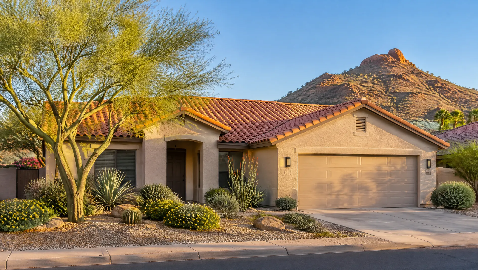 Single-story stucco ranch home in Tempe, Arizona with a freshly installed terracotta concrete tile roof, clean ridge caps and new painted fascia, a palo verde tree and desert landscaping in front, the rounded peak of a desert butte in the distance at golden hour, clear blue sky