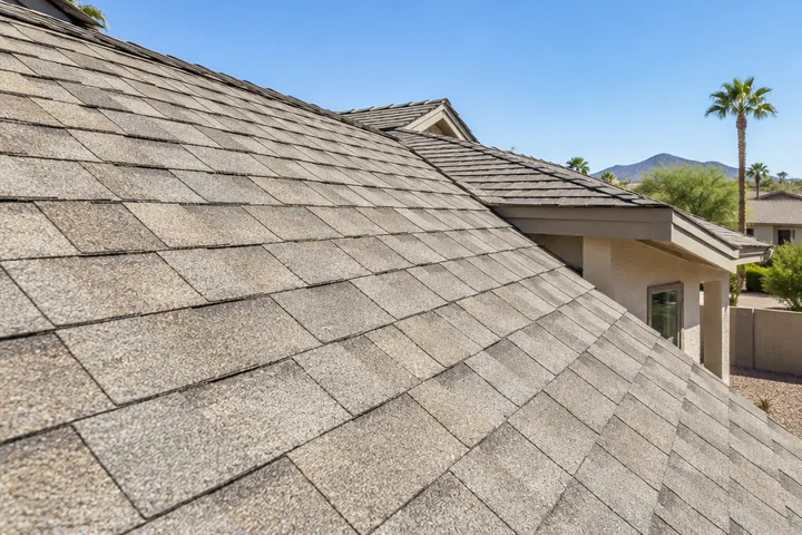 Fresh architectural asphalt shingles in a light weathered-wood color on a residential roof, close angle showing the layered texture