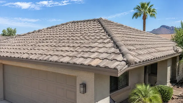 Low-slope concrete S-tile roof on an Arizona ranch home after repair: a few new replacement tiles blended in, straight courses, mortared ridge line, palm tree in the background, bright sky
